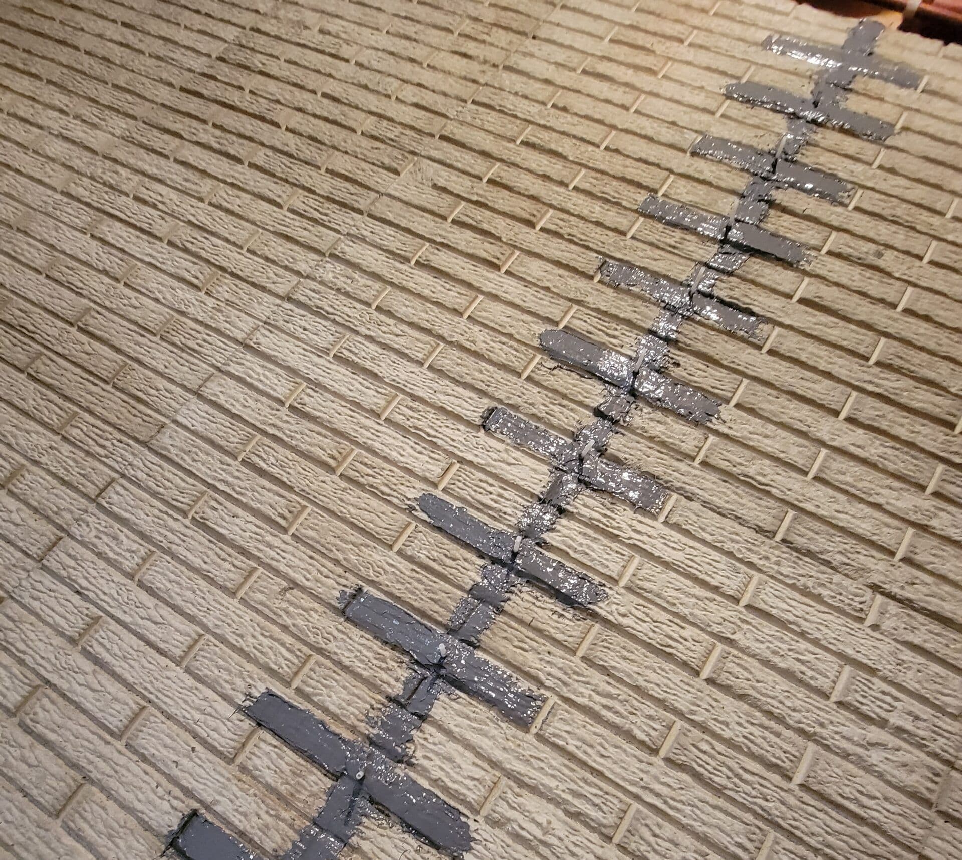 Diagonal crack in light tan brick wall with black sealant injected in the fracture line.