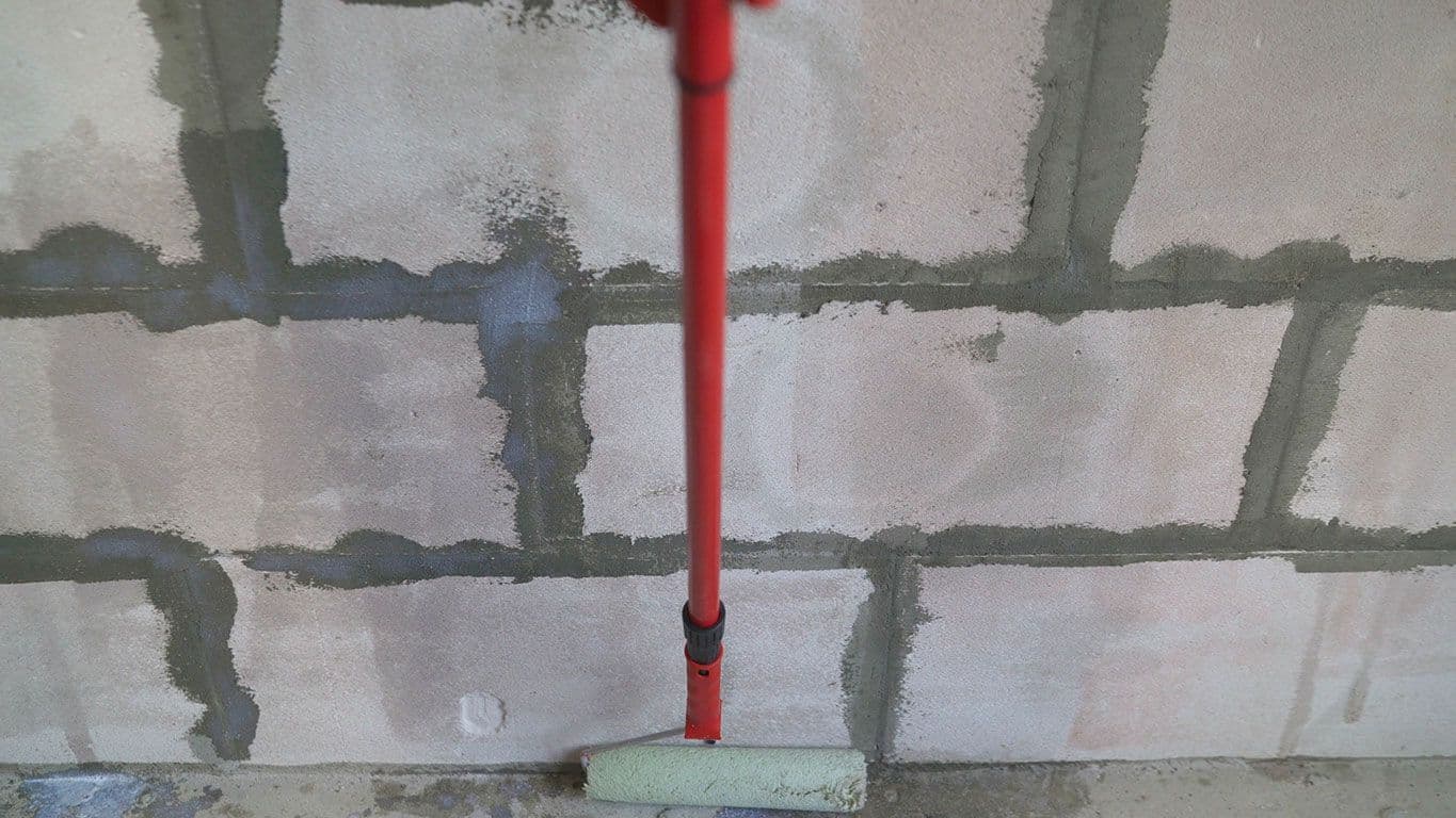 Roller with a red handle positioned against concrete block wall with dark mortar joints and sealed seams.