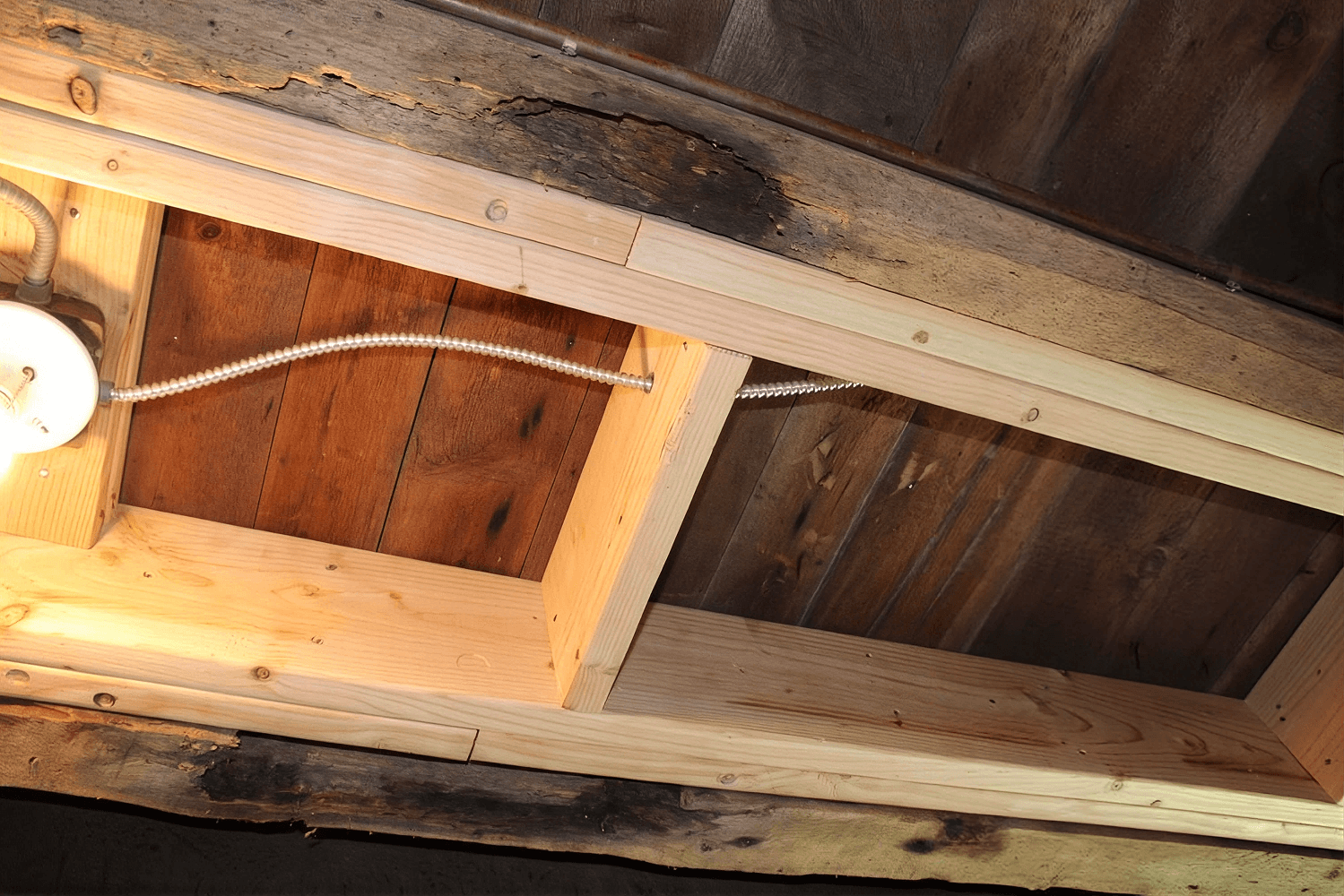 Exposed ceiling beams showing wood damage repair, with new light-colored wood sections replacing darkened or deteriorated areas.