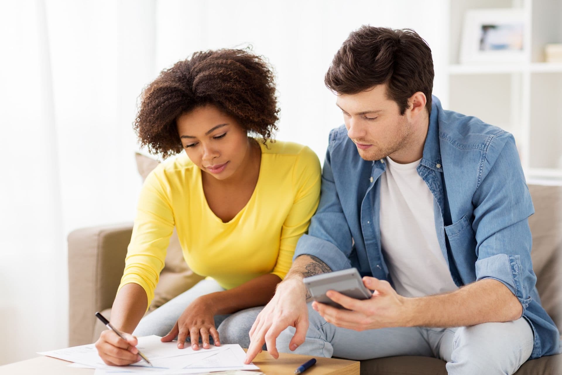 Couple reviewing documents together on a couch while planning or discussing household finances.