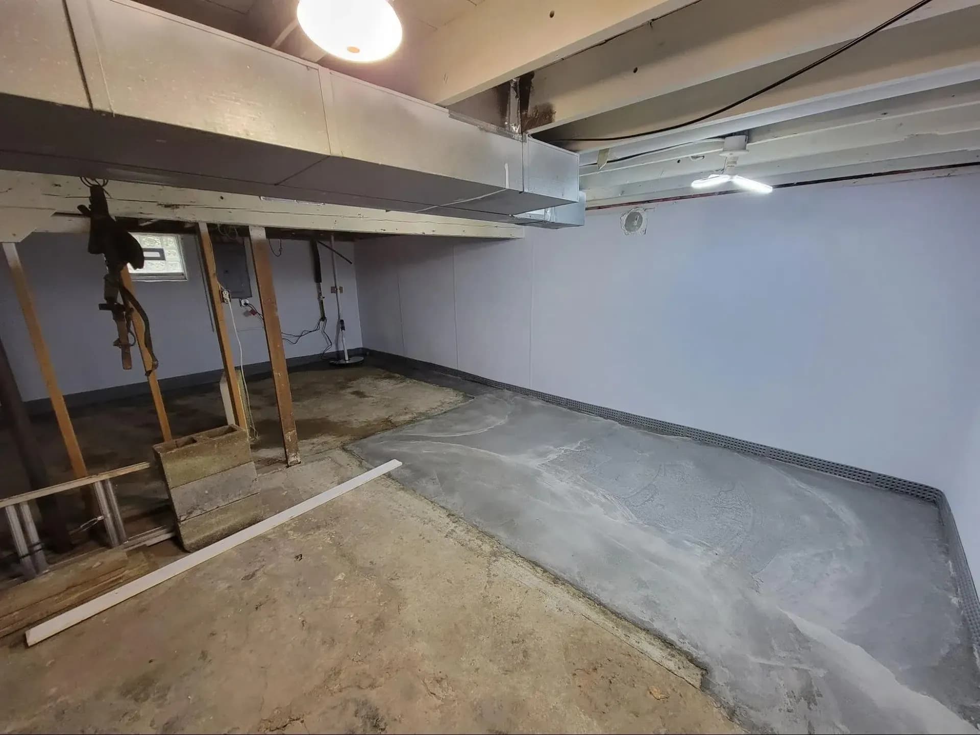 Unfinished basement space with exposed concrete floor, white walls, metal ductwork overhead, and wooden support posts under construction
