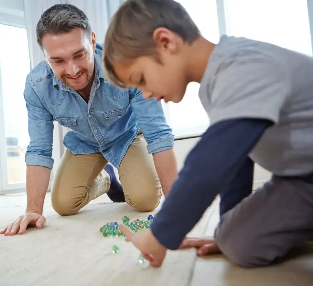 Adult and child playing with marbles on the floor together by a bright window