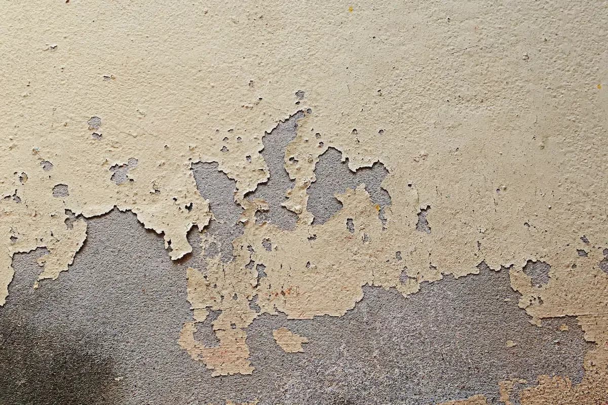 Weathered concrete surface with large patches of peeling cream-colored paint exposing dark gray underneath