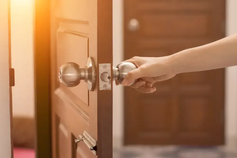 Hand opening a door by turning a spherical metal doorknob in warm sunlight