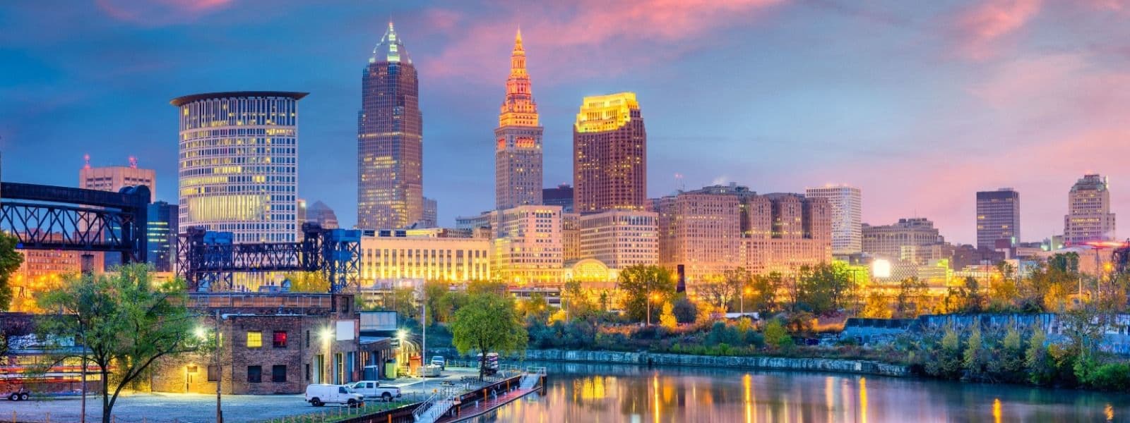 Cleveland skyline at dusk with illuminated skyscrapers, bridge, and Cuyahoga River reflecting city lights