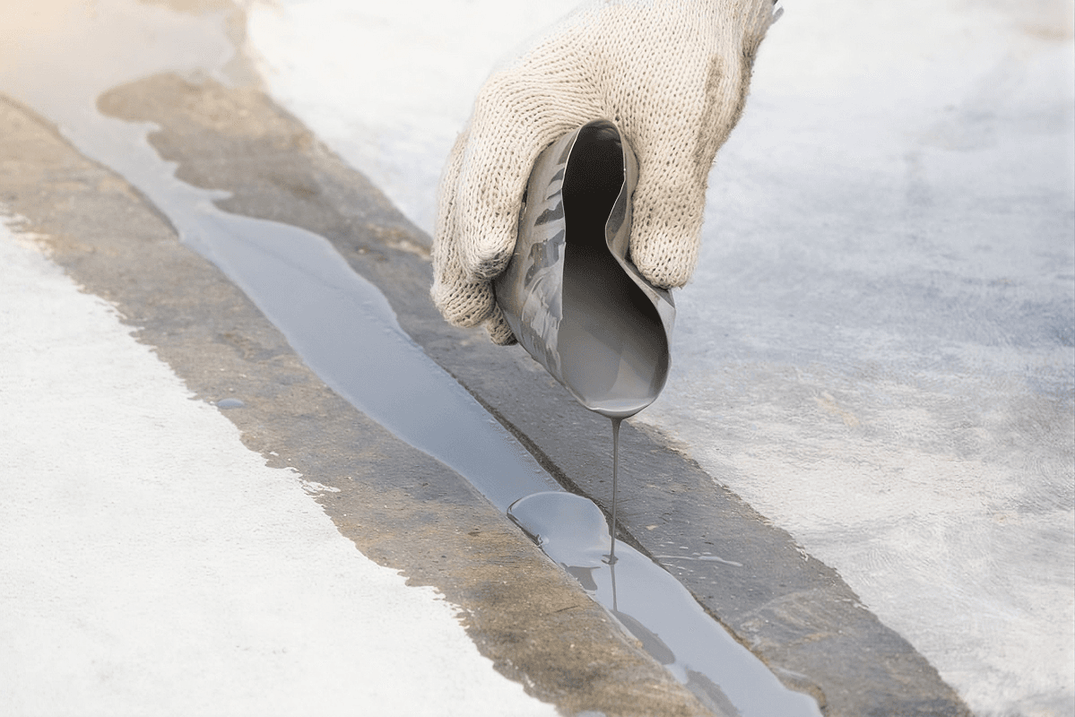 Hand in cream knit glove pouring resin sealant into a large crack in concrete.