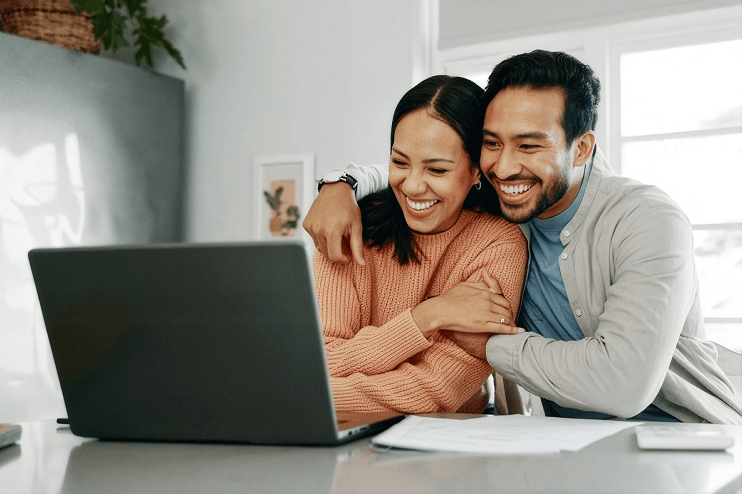 Happy couple smiling while looking at laptop screen together at home.