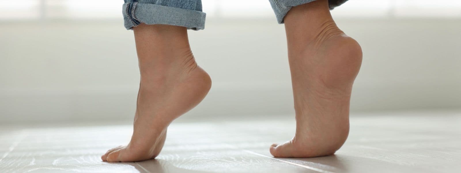 A person's bare feet on a light wooden floor wearing rolled-up denim pants.